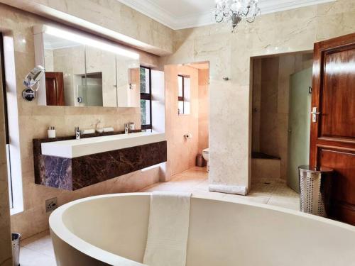 a bathroom with a tub and a sink and a mirror at The Villa Luxe Hartbeespoort Spacious Golf & Wildlife Estate in Hartbeespoort