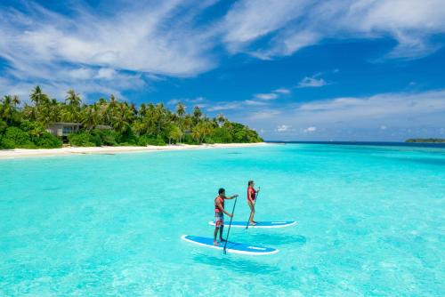 two people are standing on surfboards in the ocean at Amilla Maldives in Kihaadhoo
