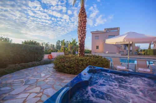 a swimming pool with a palm tree next to a house at Villa Saraliana Sandy Beach Villas - Heated Pool - Jacuzzi - Private Beach Area in Polis Chrysochous