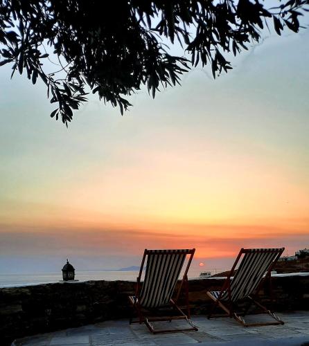 two chairs sitting in front of the ocean at sunset at Aegean living Villa in Agios Romanos