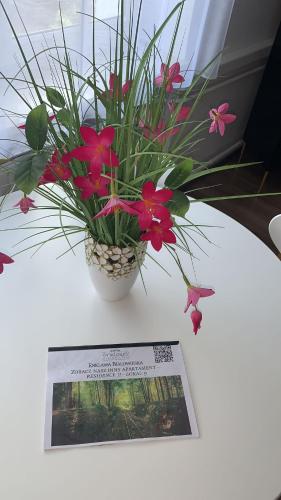 a vase with flowers on a table next to a paper at Golden Apartament Legionów in Toruń