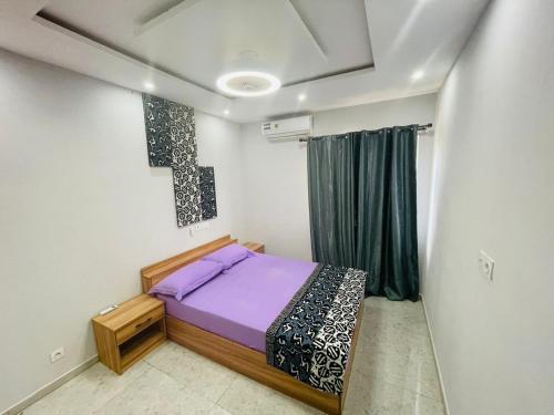 ein Schlafzimmer mit einem Bett mit violetter Bettwäsche und einem Kreuz an der Wand in der Unterkunft Appartement meublé 2chambres 1salon T3 N10 Résidence LES 11 PLURIELLES in Lomé