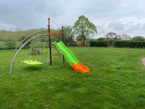 a playground with a green slide in a grass field at La ferme du paradis in Merris