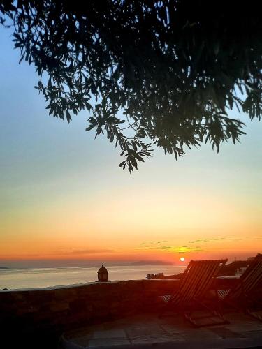 a sunset with two lawn chairs and a lighthouse at Aegean living Villa in Agios Romanos