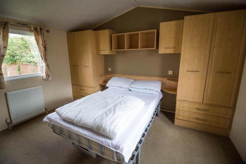 a small bedroom with a bed and wooden cabinets at 6 Berth Caravan With Free Wifi For Hire In Suffolk Ref 68073bs in Lowestoft