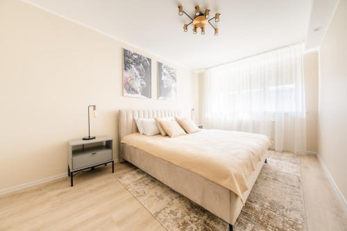 a white bedroom with a bed and a chandelier at The World is Yours seaside apartment in Liepāja