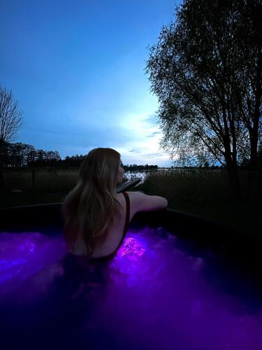 a woman sitting in a purple hot tub at Bajkowa Przystań domki nad jeziorem in Żoń