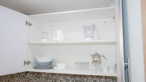 un armario blanco con platos y vasos. en Appart AYAMOUS MARINA en Kenitra