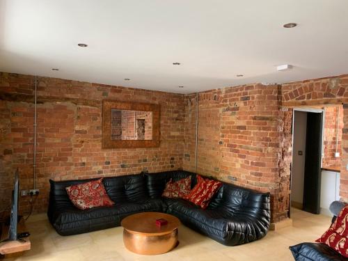 a living room with a black leather couch and a brick wall at Lavish Apartment at Montpellier Gardens in Cheltenham