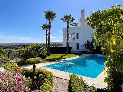 a swimming pool in front of a house with palm trees at Superior apartment for golf, sea and nature lovers in Casares