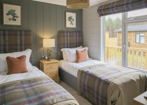 a bedroom with two beds and a window with a view at Thirlestane Woodland Lodges in Lauder