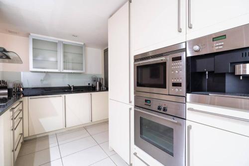 una cocina con electrodomésticos de acero inoxidable y armarios blancos en Stylish 2BRM with nice city view en Londres