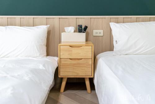 two beds with white sheets and a wooden nightstand between them at 台東市區維拉包棟民宿 附廚房及電動麻將 in Taitung City