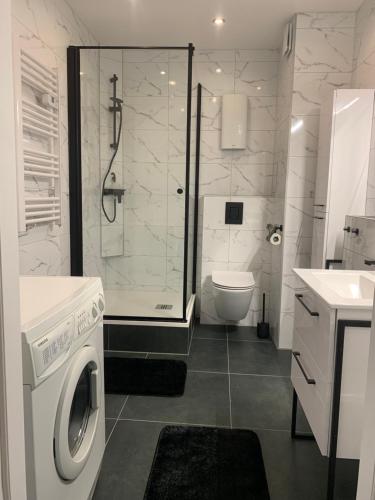 a white bathroom with a shower and a washing machine at Marias Apartment in Międzyzdroje