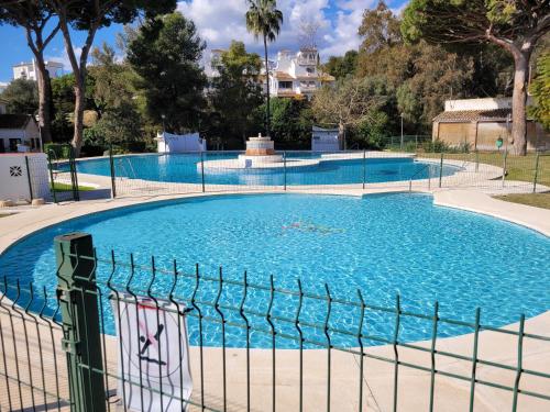 uma grande piscina com água azul atrás de uma cerca em Bonita casa adosada en esquina em Marbella