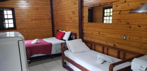 two beds in a room with wooden walls and windows at Chalés internacional l in Paraty
