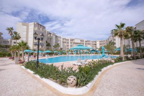 a resort pool with chairs and umbrellas and palm trees at 2 Bedrooms apartment swimming pool in Monastir