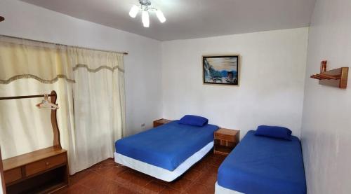 a bedroom with two beds with blue sheets and a window at Hostal Poseidon - Neptuno in Puerto Villamil