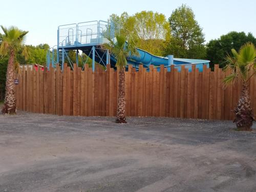 um parque infantil com um escorrega azul atrás de uma cerca de madeira em Mobilhome bien équipé et climatisé em Mimizan