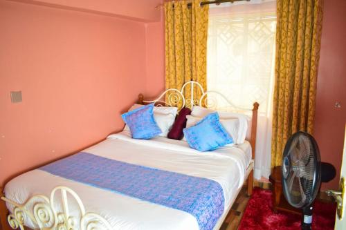 Schlafzimmer mit einem Bett mit blauen Kissen und einem Ventilator in der Unterkunft Cozy 2 bedroom in a family home in Nakuru