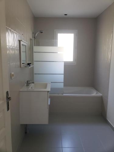 a white bathroom with a tub and a sink and a window at Chambres in Yvré-le-Pôlin