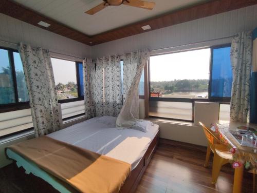 a bedroom with a bed and a table and windows at Diamond Cottage in Alibaug