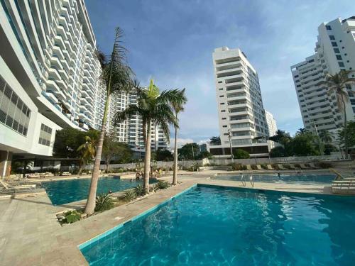 a swimming pool with palm trees and buildings at Reserva del Mar - Apto con vista al mar in Santa Marta