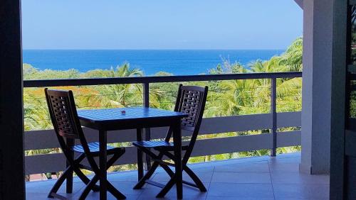 einen Tisch und zwei Stühle auf einem Balkon mit Meerblick in der Unterkunft Hotel - Résidence Habitation Grande Anse in Deshaies