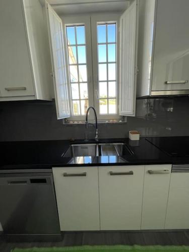 a kitchen with white cabinets and a sink and two windows at Casa da Celeste in Vale do Pereiro