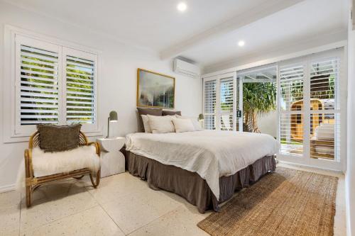 a bedroom with a bed and a chair and windows at Sirens in Byron Bay