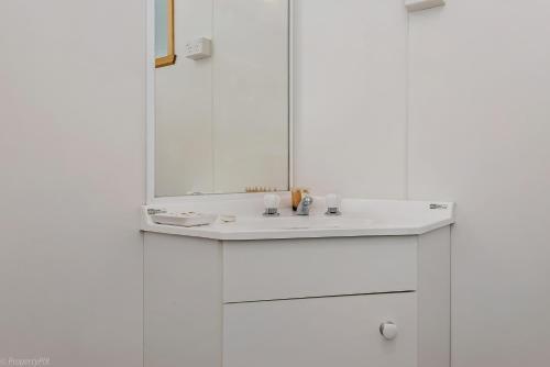 a white bathroom with a sink and a mirror at Hobart Bush Cabins in Kingston