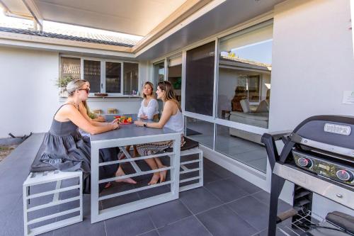 a group of women sitting at a table on a patio with a grill at Bokarina Seaside Escape - Only steps to the Beach in Kawana Waters