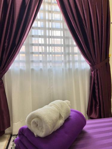 a white towel laying on a bed in front of a window at RAINA MUSLIM FRIENDLY HOMESTAY Perlis in Arau