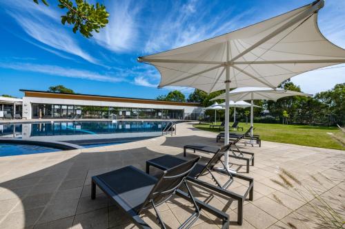a patio with chairs and umbrellas next to a pool at Mercure Kooindah Waters Central Coast in Wyong
