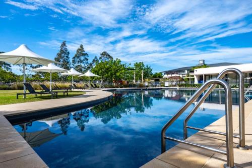 a swimming pool with umbrellas and chairs next to a building at Mercure Kooindah Waters Central Coast in Wyong