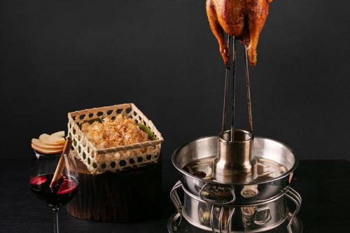 a person holding a piece of food in a pot and a glass of wine at JM Marvel Hotel & Spa in Hanoi