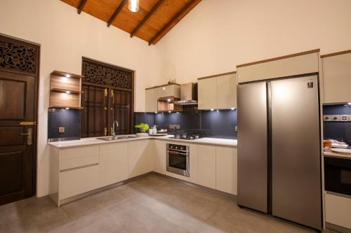 cocina con armarios blancos y nevera de acero inoxidable en Balumgala Estate Bungalow Kandy, 