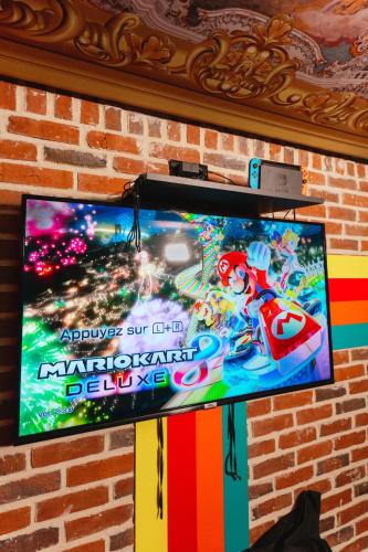 a flat screen tv hanging on a brick wall at Capsule Art Déco - Jacuzzi - Netflix - Home Cinéma - Arcade de jeux & Nintendo switch - 2 chambres - Filet suspendu in Valenciennes