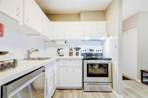 a white kitchen with a sink and a stove at Roomy Top Floor at Stampede w Free Parking and AC in Calgary
