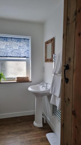 a white bathroom with a sink and a window at Castell in Llangwyllog