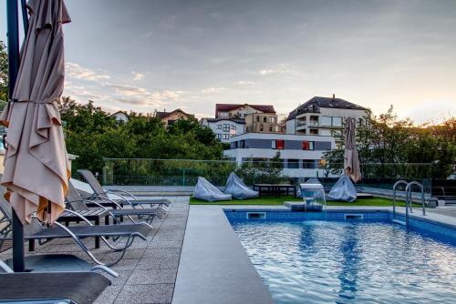 a swimming pool with chairs and umbrellas next to a building at Panorama Deluxe Aparthotel in Cluj-Napoca