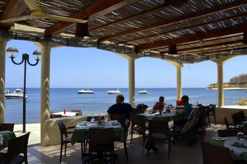 people sitting at tables in a restaurant overlooking the ocean at Horizon Apartments Gozo in Marsalforn
