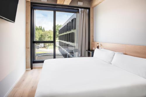 a bedroom with a white bed and a large window at B&B HOTEL Guimarães in Guimarães