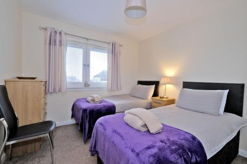 a bedroom with two beds with purple sheets and a window at Caledonia Newhills Apartment in Aberdeen