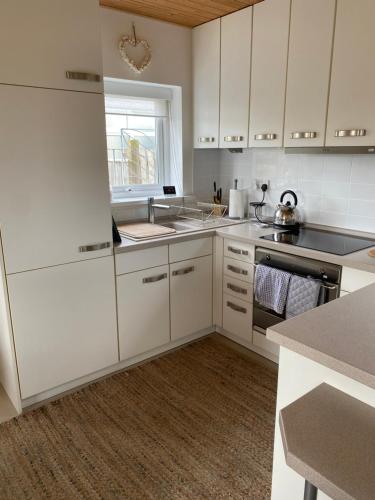 a white kitchen with white cabinets and a window at Moonstone in Beadnell
