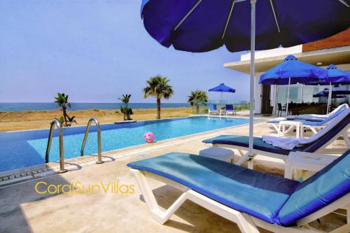 a swimming pool with two chairs and an umbrella at Blue - Beach Front Spectacular Villa Sleeps 10 in Argaka