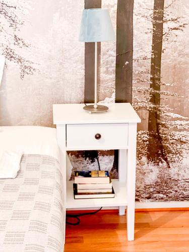 a white nightstand with a lamp on it next to a bed at Ilona Apartments -"Home Away From Home" in Kotka