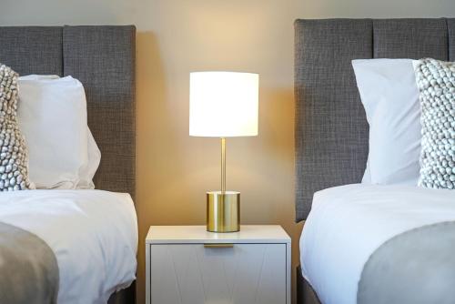 a lamp on a night stand next to two beds at Grange House with Free Parking, Garden, Superfast Wifi and Smart TVs with Netflix by Yoko Property in Northampton