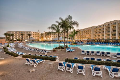 un complexe avec une piscine, des chaises et des palmiers dans l'établissement db Seabank Resort + Spa All Inclusive, à Mellieħa