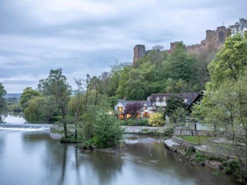 a house next to a river with a castle in the background at The Marches, Ludlow in Ludlow